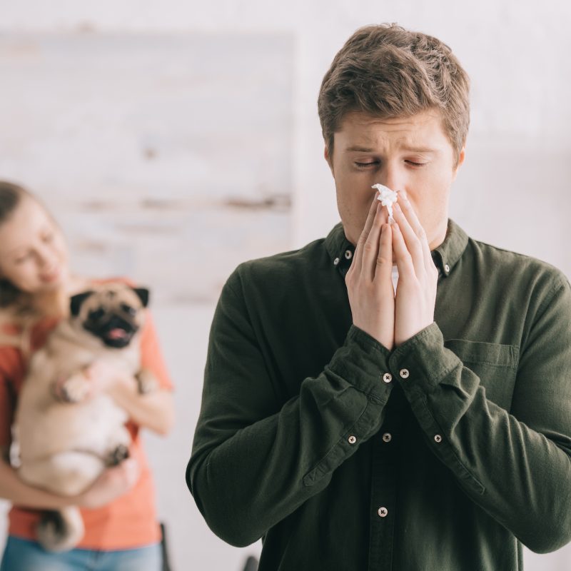 selective focus of man sneezing in tissue with closed eyes while standing near woman with dog
